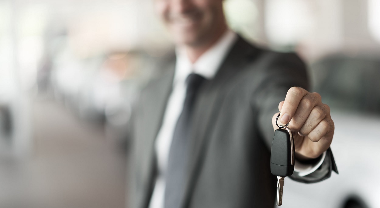 65343879 - smiling car salesman handing over your new car keys, dealership and sales concept